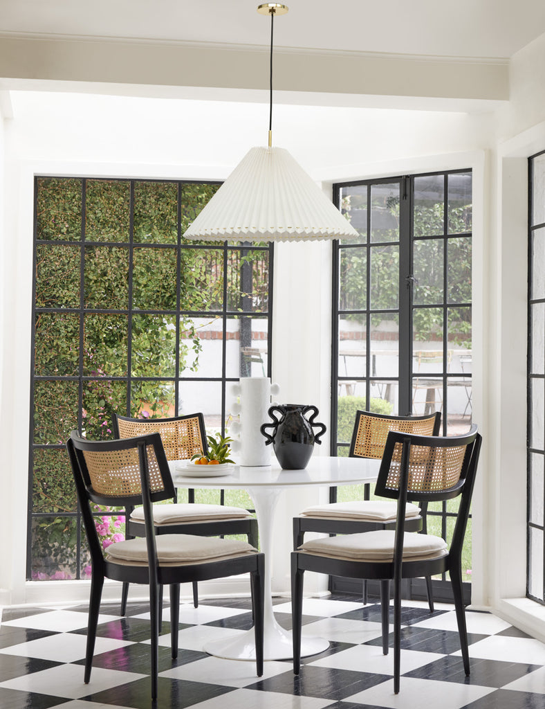 A black and white checkerboard floor set a vintage tone in this kitchen dining nook. Four black and rattan padded chairs surround a round white table.