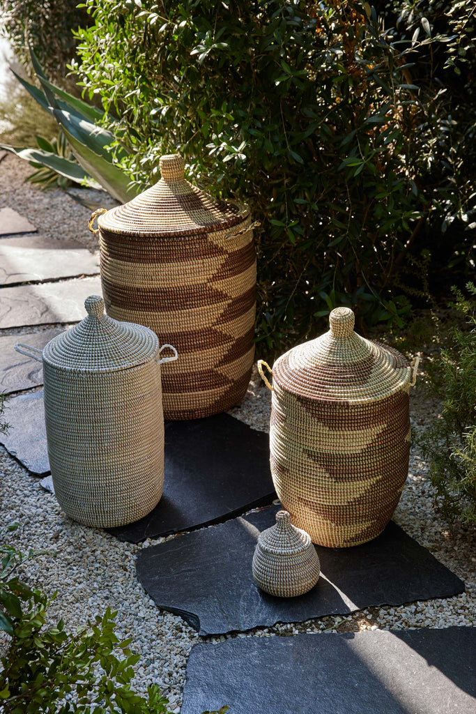 Two Expedition Subsahara Astou storage baskets in medium and large sizes and Ndeye storage baskets in medium and small sizes  sit on a paver path outside.