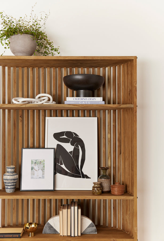 A curved wooden bookcase holds a black and white portrait of a woman and decorative vases and accessories.