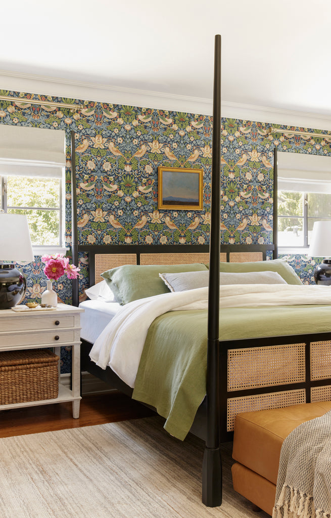 Morris & Co. Strawberry Thief Wallpaper hangs in this bedroom with a black and cane four-poster bed  with sage green bedding.