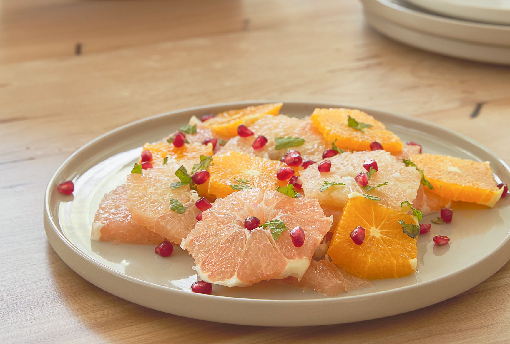 A round white Casafina dinner plate holds a summer citrus fruit salad of sliced oranges, pomegranate seeds and mint.