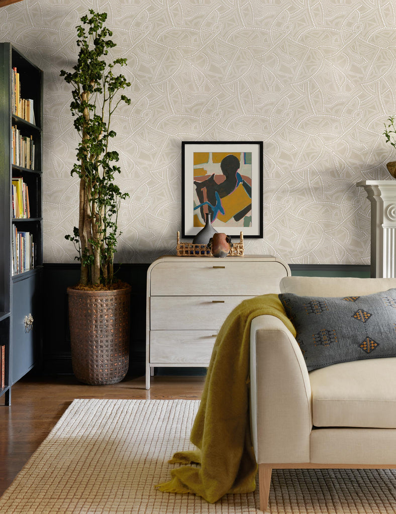 The neutral Heritage Wallpaper by Malene Barnett features textured dots and abstract shapes in chalky white colors. The wallpaper contrasts against dark green wainscotting in a modern and colorful sitting room.