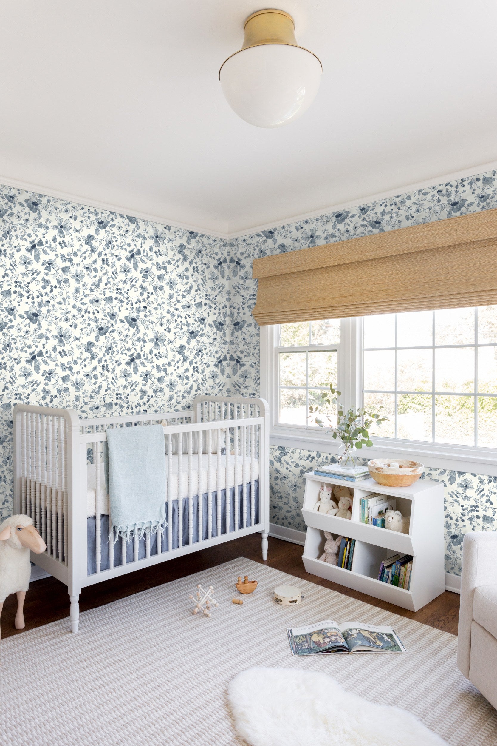 A blue floral wallpaper sets a sophisticated tone for this nursery, with a white crib, neutral striped rug and toys spread on the rug.