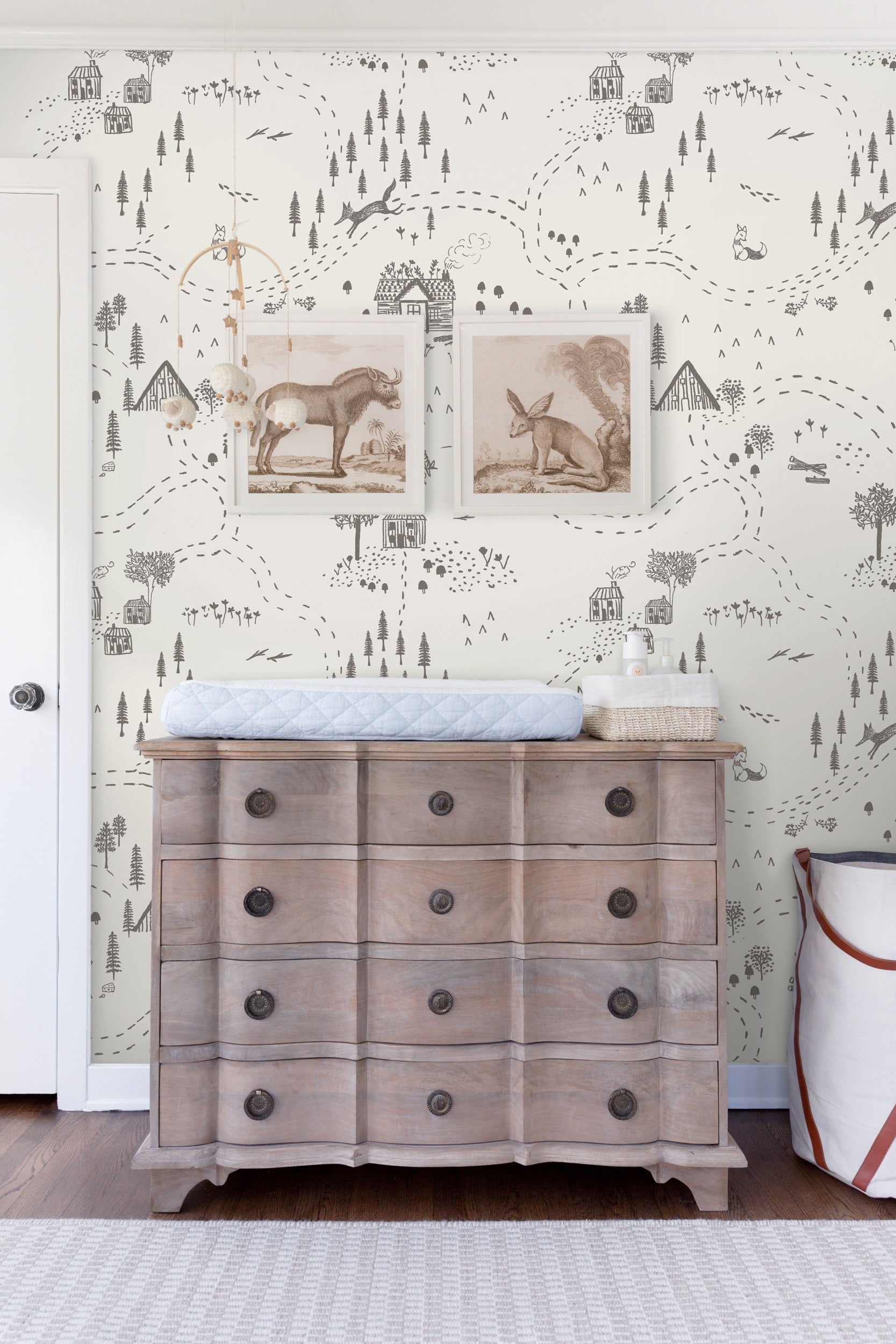 The rustic Through the Woods black and white wallpaper from Rylee + Cru is a backdrop to a whitewashed wood dresser with a changing pad on top in this nursery.