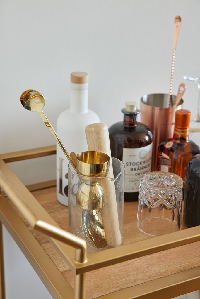 A wood and gold bar cart holds some of Hawa Hassan's favorite ingredients to make a cocktail, including a jigger, a muddler, a strainer and a mixing spoon, along with a crystal glass.