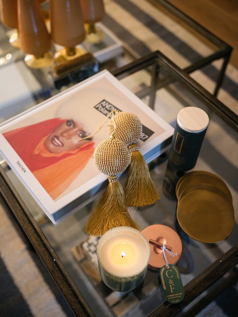 Two fringed and beaded gold ornaments lay on top of a book on Rashida Banks' coffee table. A lit candle sits next to it.