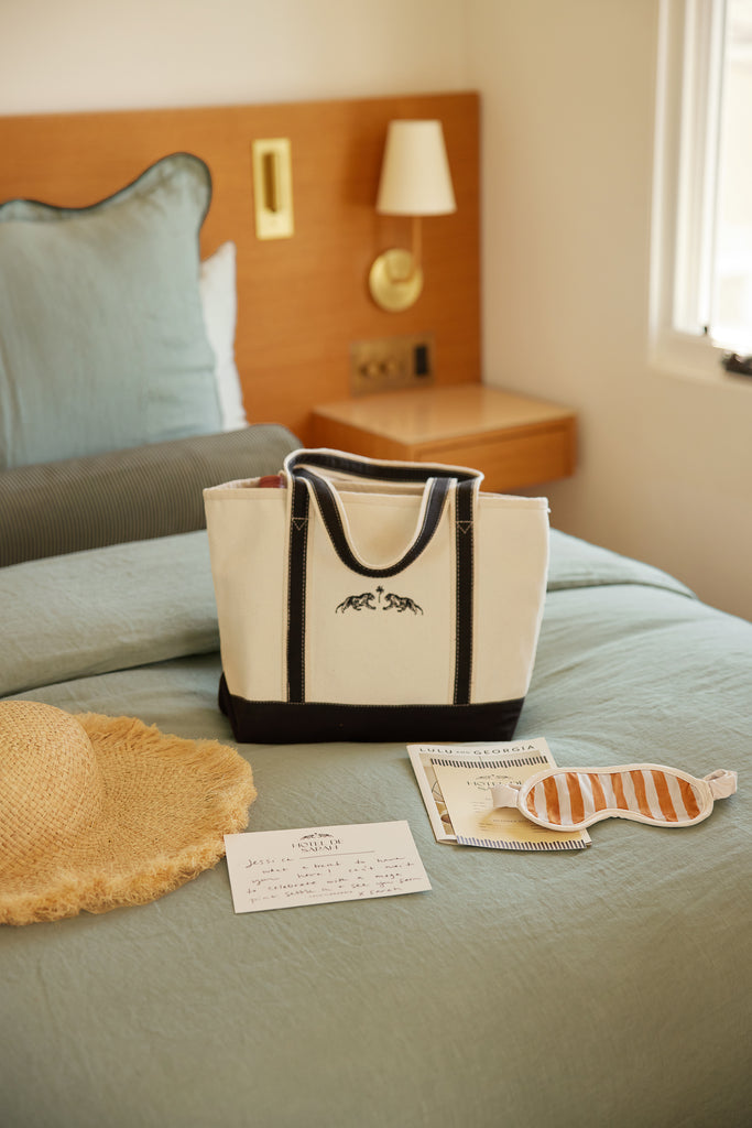 Canvas tote bag, sleeping mask and straw beach hat laid out on a bed.