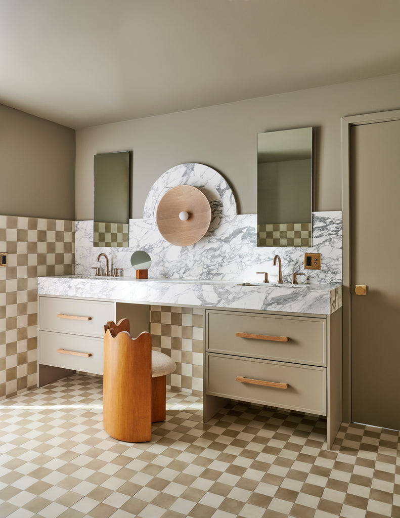 A vintage-inspired brown and white checkerboard tiled bathroom has the wood and upholstered Ripple vanity chair and a putty brown painted vanity with marble countertop.