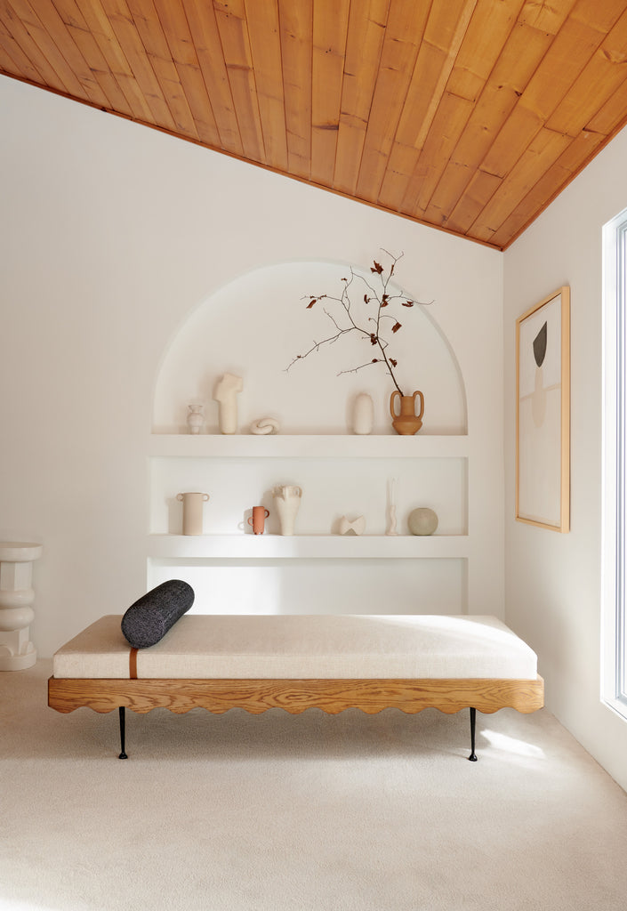 A low daybed with rippled wooden base and an ivory cushion sits in front of a built-in arched bookcase.