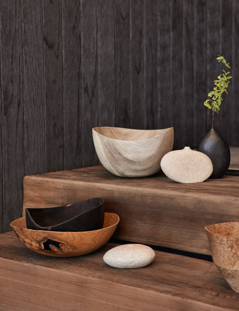 Namu Home Goods carved wooden bowls, vases and vessels sit on a wooden platform.