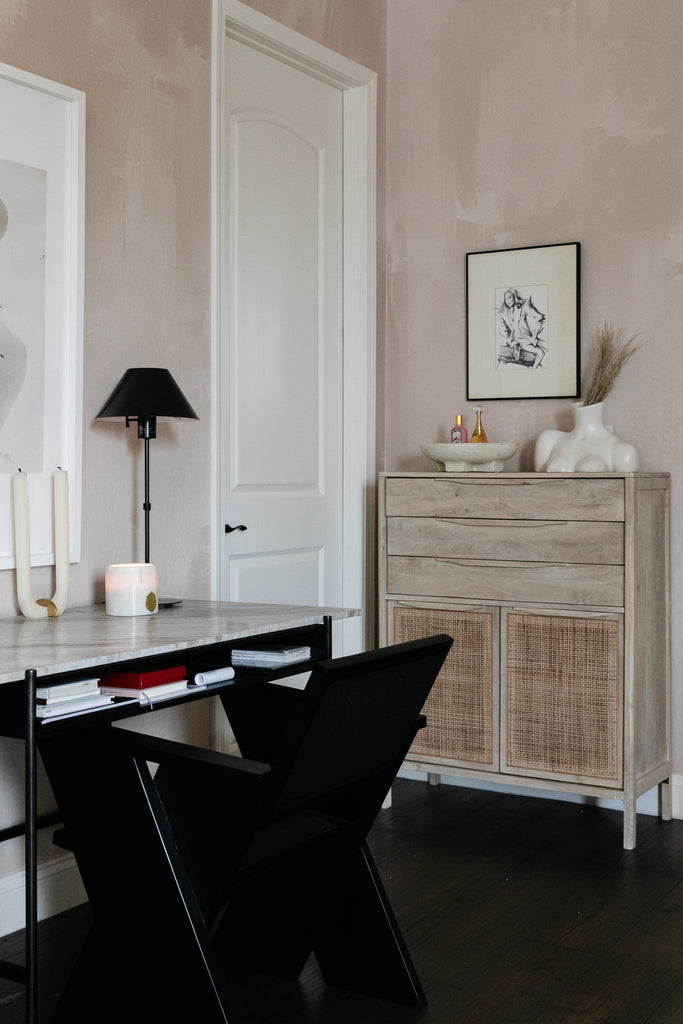 A black desk chair sits at a marble-topped desk in Chriselle Lim's bedroom. Next to the desk is the light wood Hannah Dresser featuring cane paneled doors.