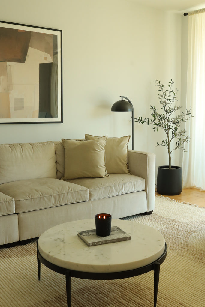 A light squared arm sofa sits atop a Nomad neutral geometric woven rug. A small round marble topped Arteriors Kelsie coffee table sits in the middle of the room. An abstract painting hangs above the sofa.