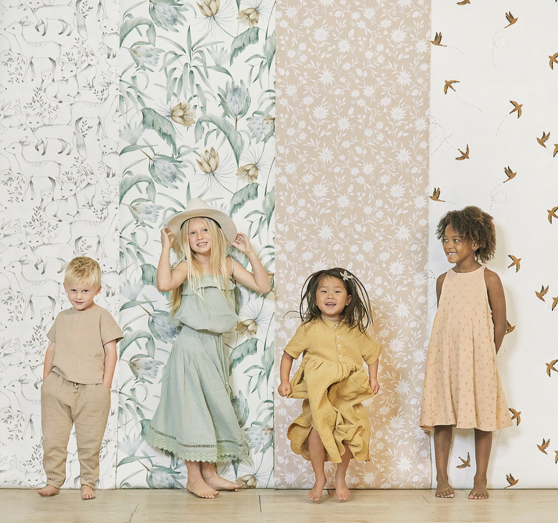 Four children stand in front of Rylee + Cru wallpaper samples rolled out on a wall.