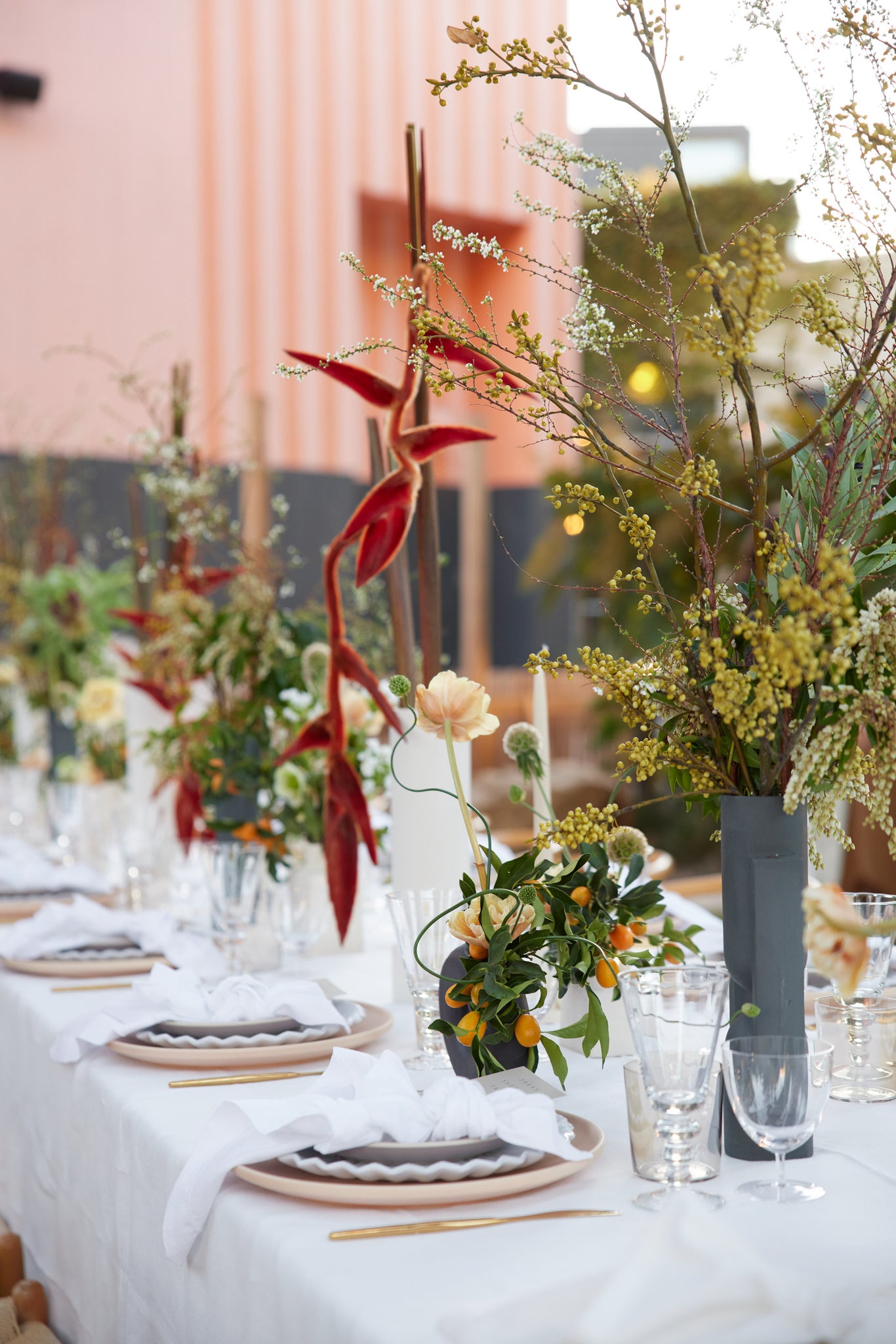 Modern floral arrangements of varying heights line an outdoor dinner table celebrating the Sarah Sherman Samuel x Lulu and Georgia collection. Place settings and glasses line the table.