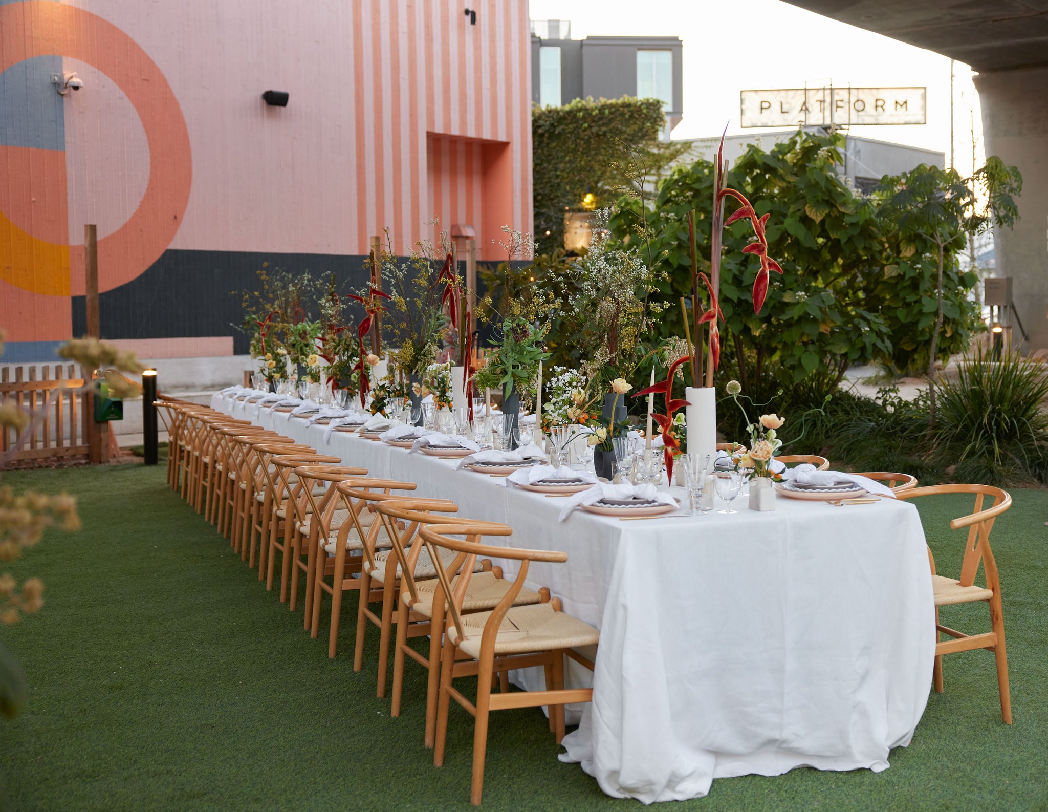 A long dinner table covered in a white table cloth, place settings and modern flower arrangements of varying heights sits outside of the Sarah Sherman Samuel x Lulu and Georgia pop-up shop in LA.