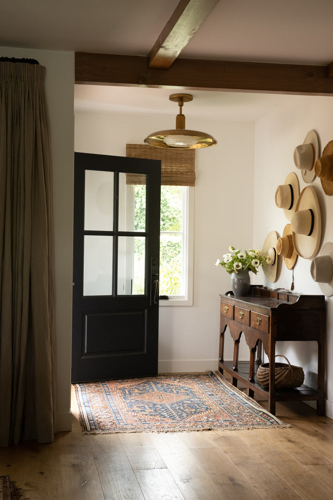 The entryway to Sarah Solis' home has a red and blue patterned Persian rug and an antique console table with three drawers. Straw hats hang above the table for a unique art installation.