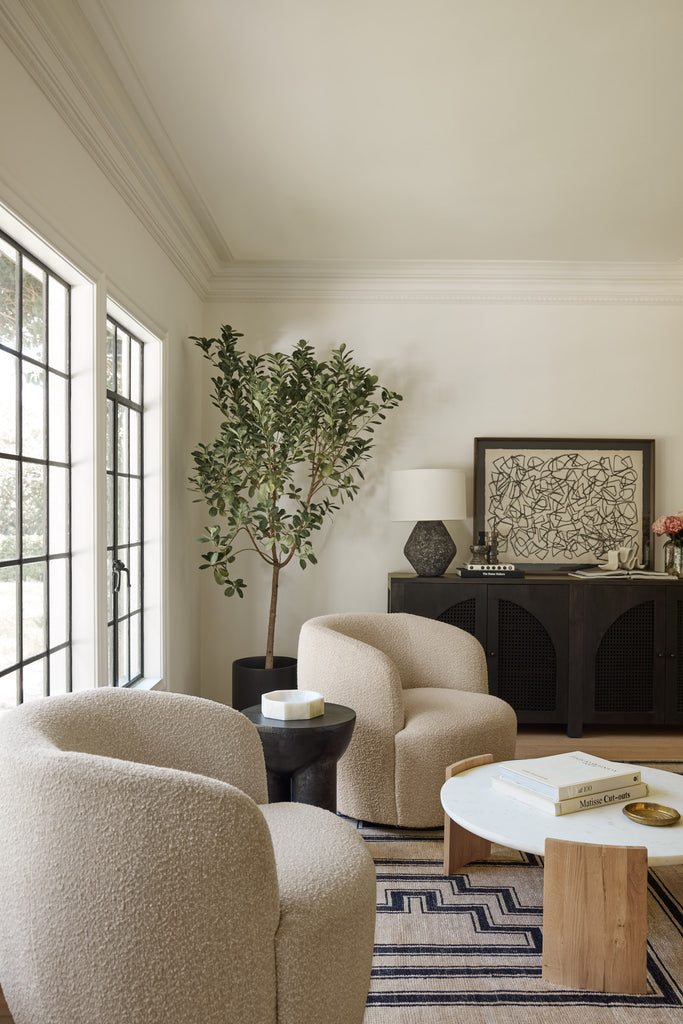 Two natural-colored boucle barrel swivel chairs sit upon the neutral and black geometric patterned Senna rug in a casual seating arrangement. A small round dark wood table sits between the chairs and a marble and wood round coffee table sits on the rug.