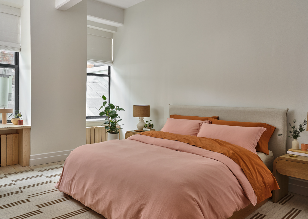 An oatmeal linen slipcovered headboard is a backdrop for peach and rusty red bedding. The offset striped Stripe Break Rug by Sarah Sherman Samuel grounds the space.