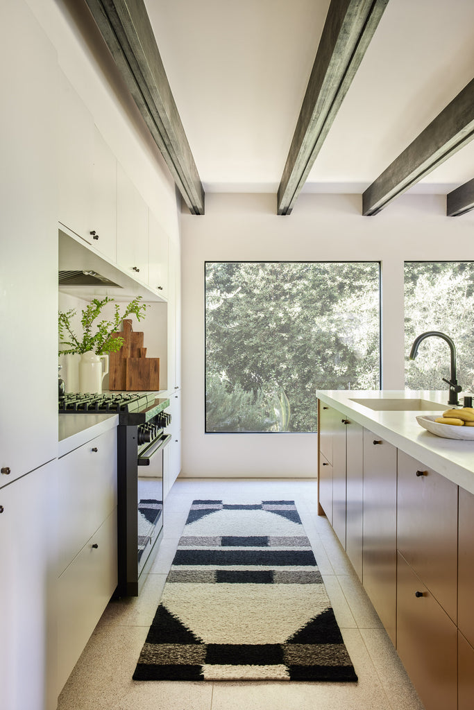 A geometric black, gray and ivory runner rug sits in a modern kitchen and large picture windows.