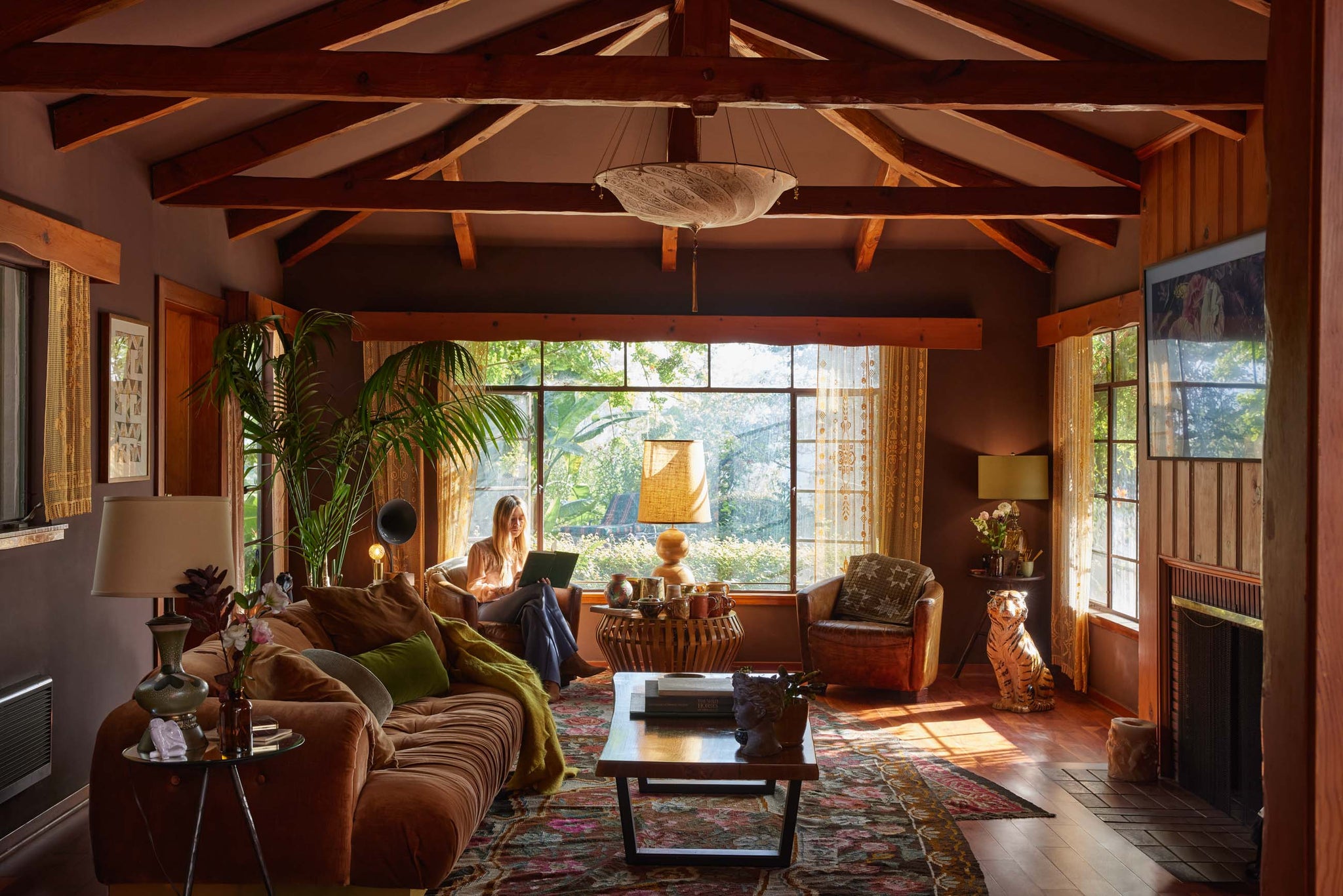 Chase Cohl sits in a round brown leather arm chair in the back of her cozy and dark living room. Another matching chair with a round reeded end table sits between the two chairs and a tiger statue sits to the chair's right. A plush deep brown velvet tufted sofa sits in the middle of the room across from a fireplace.