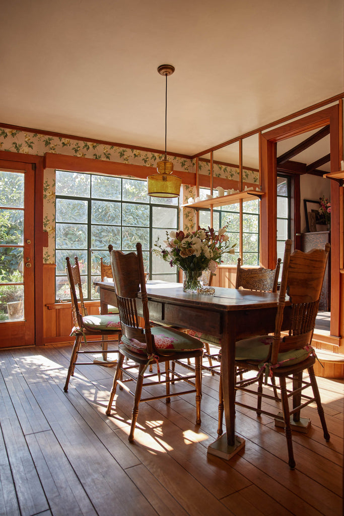 An amber glass pendant light hangs above a country-style wooden rectangular kitchen table and ornately carved wooden dining chairs.