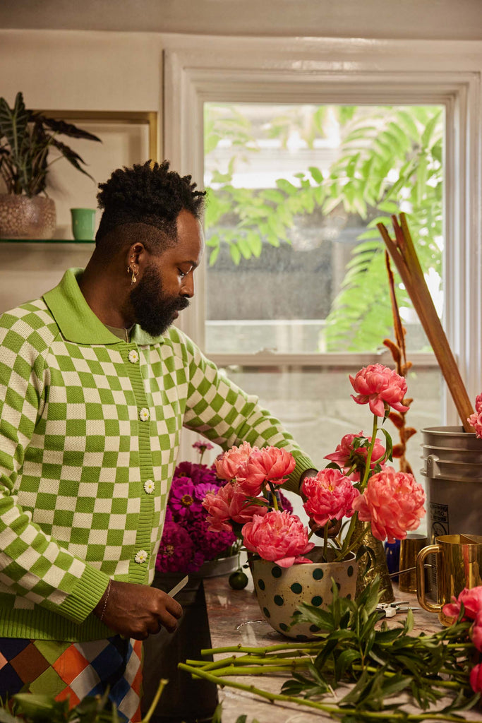 Maurice Harris arranges cut pink peonies in a white and black polka dot vase in his kitchen.