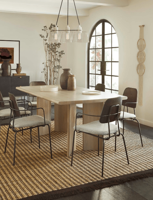 A Studio Nom wall hanging hangs in a modern dining room with a light wood table and six wood and metal dining chairs with an ivory linen cushion.