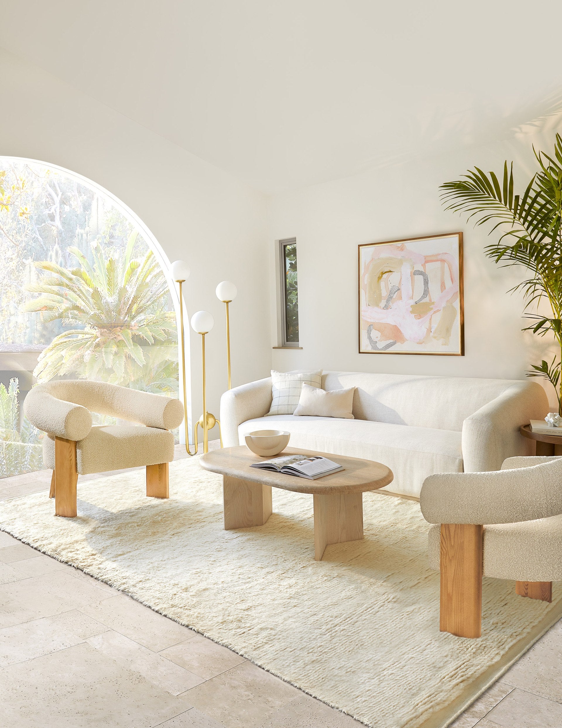 The rounded Harlowe sofa anchors this living room and is offset with two rounded Celeste neutral boucle accent chairs, a light wood coffee table, and gold floor lamp.