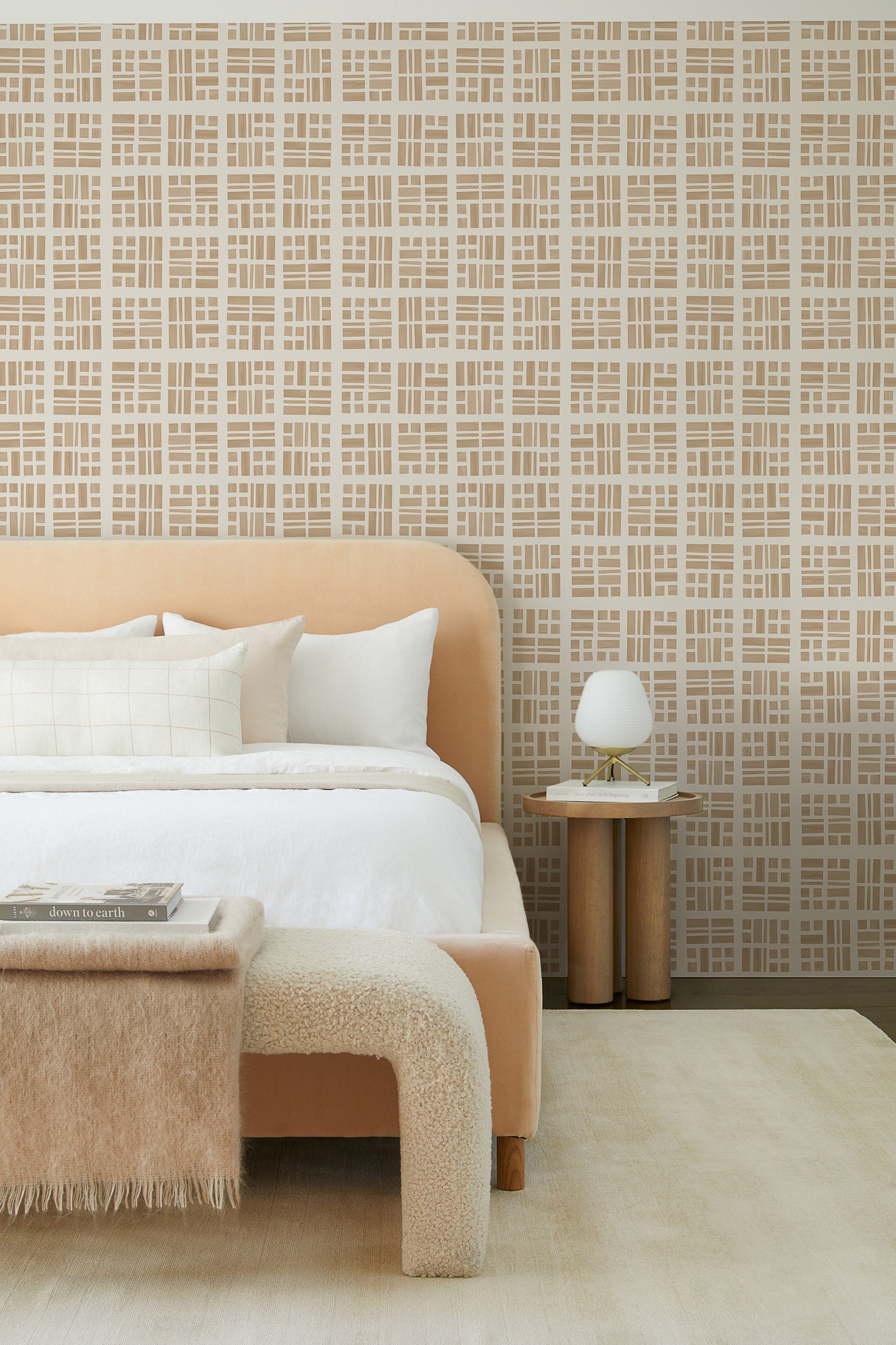 A bold taupe and natural grid Takeo wallpaper sets the tone for this bedroom with a buff-colored Solene upholstered platform bed with neutral bedding and a neutral boucle Tate bench at the foot of the bed.