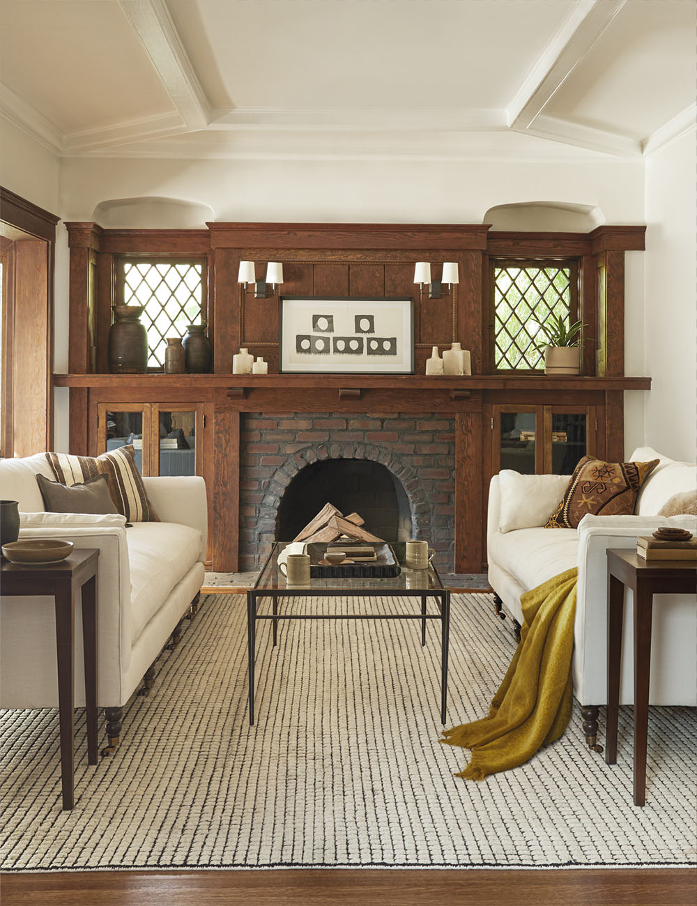 The subtly checked black and neutral Uma rug grounds this craftsman-style living room with two ivory sofas facing each other in front of a wooden fireplace.