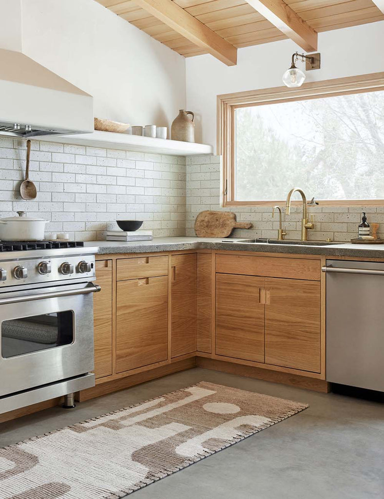 The Abode tan and cream geometric runner rug by Elan Byrd lays against wooden counters in a modern open kitchen.