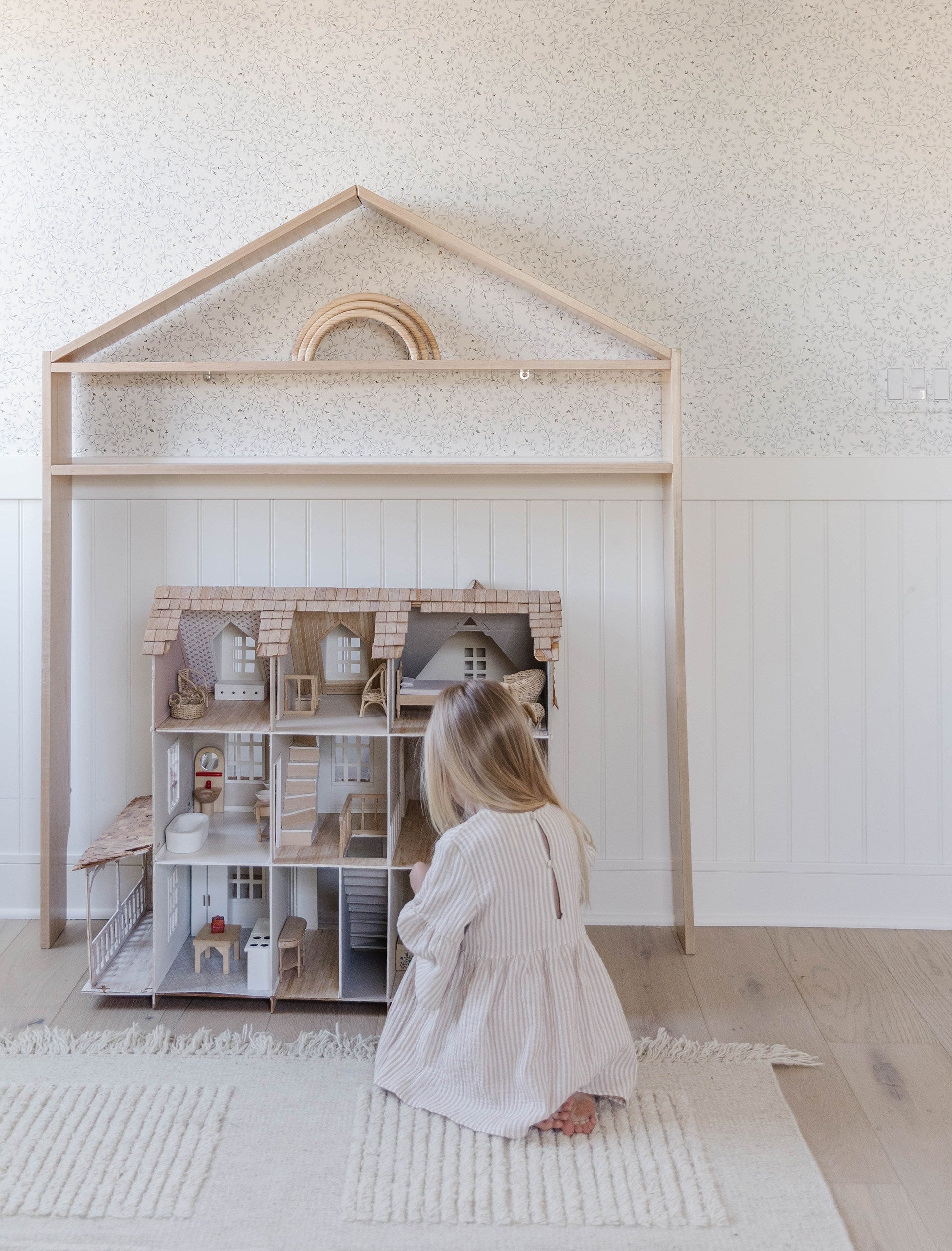 Dainty floral wallpaper is the background to a child playing with a dollhouse.