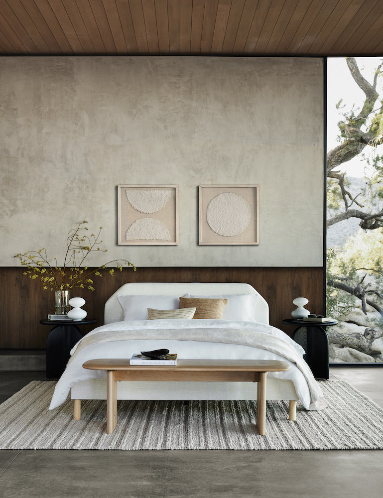 A neutral bedroom has a white upholstered angled headboard with white bedding against a dark wood wainscotting and light gray-brown wall treatment.