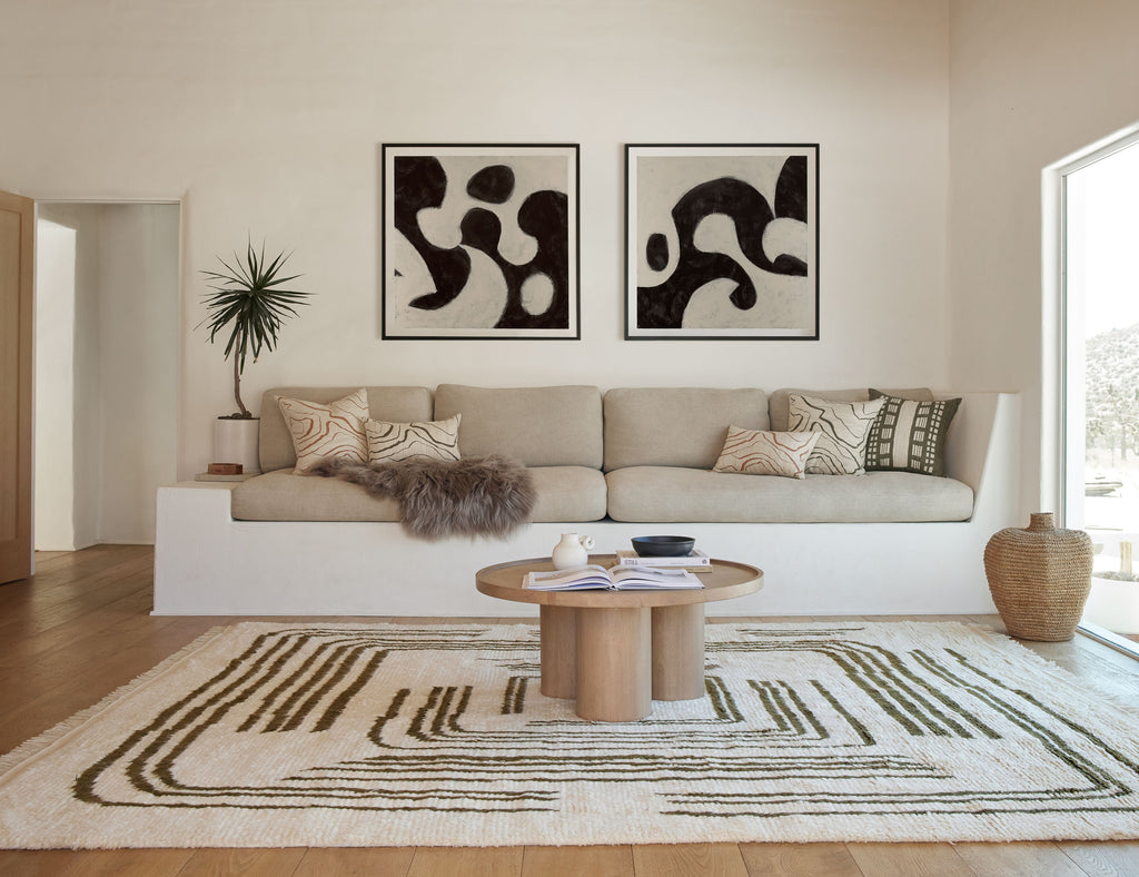 The neutral-hued Earth Maze Moroccan Shag Rug designed by Elan Byrd sis in a modern living room with a built-in white stucco sofa with tan linen cushions and neutral colored throw pillows.