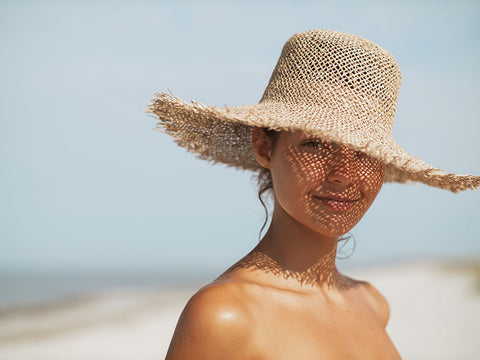 Млада жена с плажна шапка предпазва кожата си от вредното влияние на слънцето 
