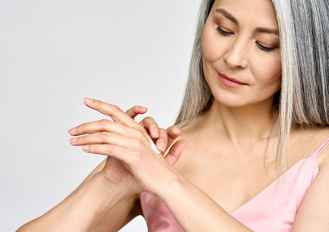 Жена на средна възраст използва крем за ръце за премахване на старчески петна.