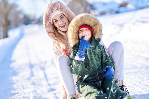 Майка и дете се забавляват в снега, като предпазват кожата си с крем за лице.