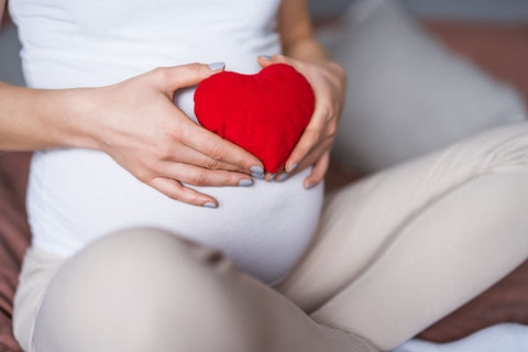 Бременна жена, държаща червено сърце в ръцете си.
