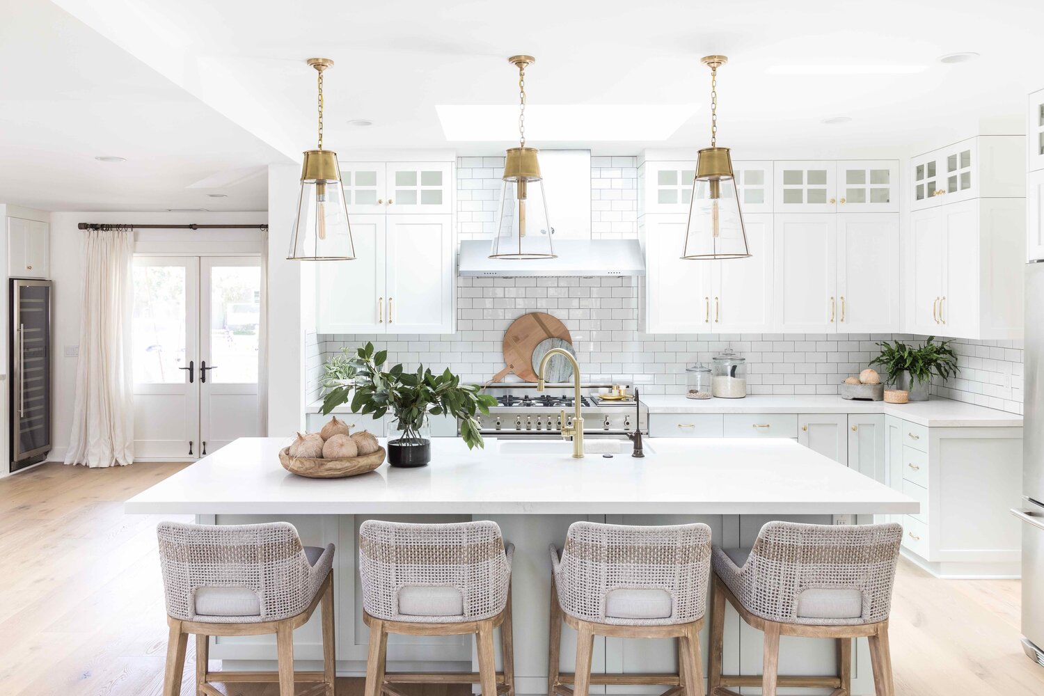 Kitchen with white cabinets and brushed gold cabinet pulls. Wood stools at white island and gold and brass fixtures. 