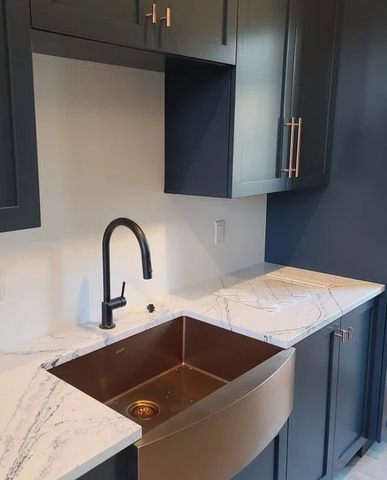 Kitchen with copper sink and antique copper cabinet pulls. Navy cabinets and a white countertop