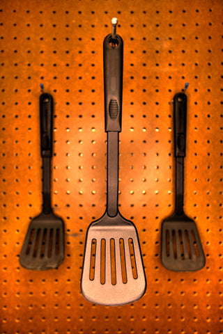 Kitchen pegboard with three spatulas hanging from pegs