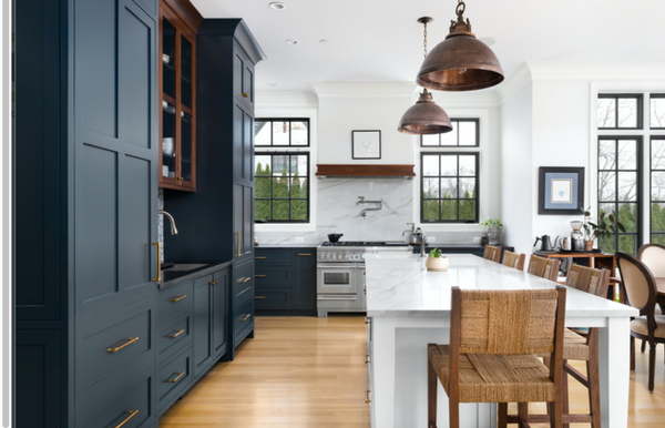 Modern kitchen with navy cabinets, white island and copper accents. The kitchen has copper cabinet pulls, copper pendant lights and copper shelving. There is stainless steel range and warm honey hardwood floors. 