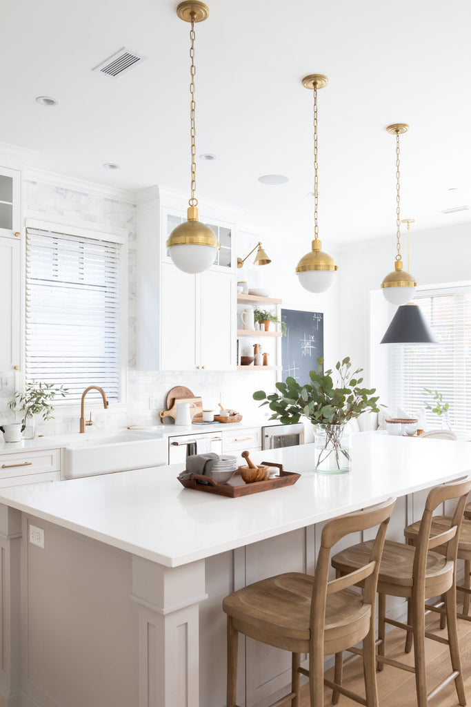 Bright kitchen with brushed brass cabinet knobs and pulls on white shaker cabinets. Gold fixtures and a wood island are also featured. 