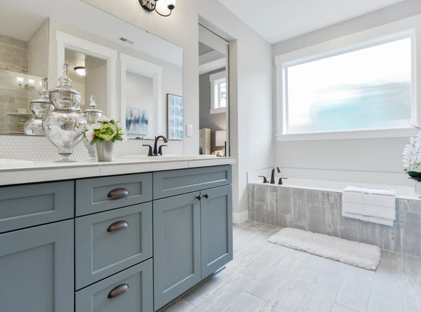 bathroom with blue vanity and white counter tops. There is a white tub and all the cabinet hardware and fixtures are oil rubbed bronze.