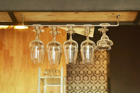 clear wine glasses hanging from a metal rod attached to a wooden cabinet