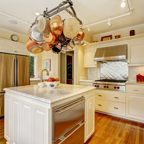 Copper and metal pots and pans hanging over a kitchen island in a contemporary kitchen with white cabinets