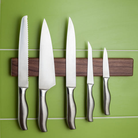Stainless steel knives on a brown magnetic knife strip agains a green kitchen wall