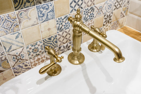 brushed brass kitchen faucet on white sink with pastel antique tiles on wall