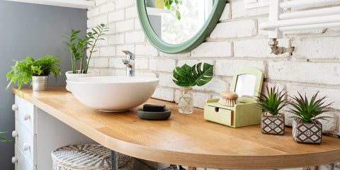 Bathroom counter with a white bowl sink, wood countertop and lots of plants