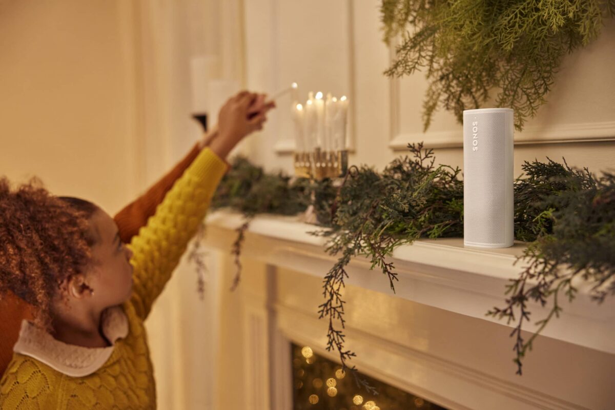 Child lighting candles on fireplace next to white Sonos Roam